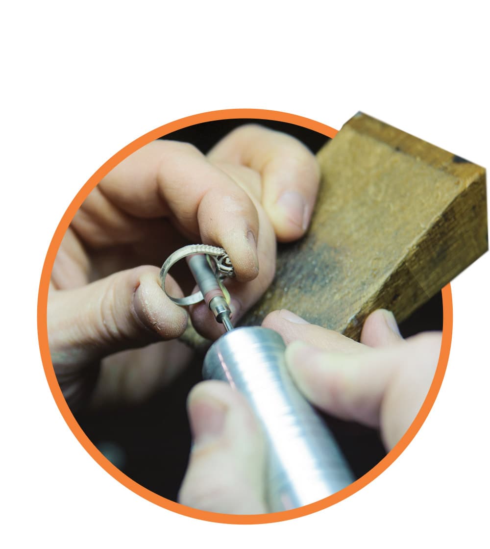 Jeweler hand-stamping metal and setting stones at a workbench
